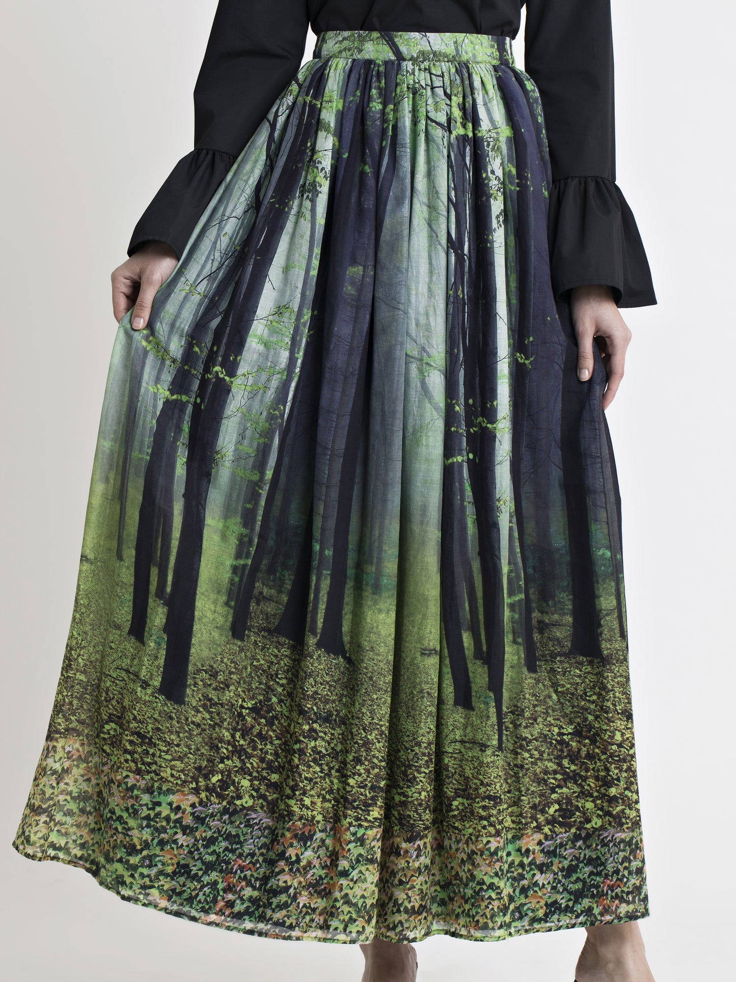 Lower body view of a female model wearing a black cotton flared cuff dress shirt, and a long cotton forest print gathered skirt, from the RÉZO women's collection.